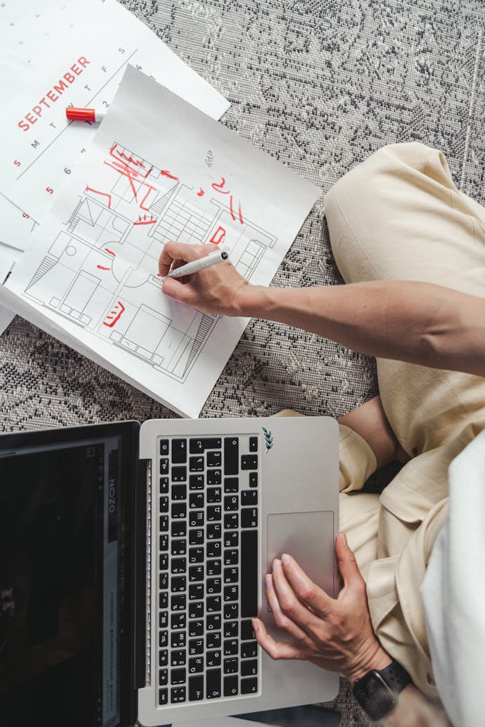 about-01 Overhead view of a person sketching floor plans next to a laptop on a carpet.